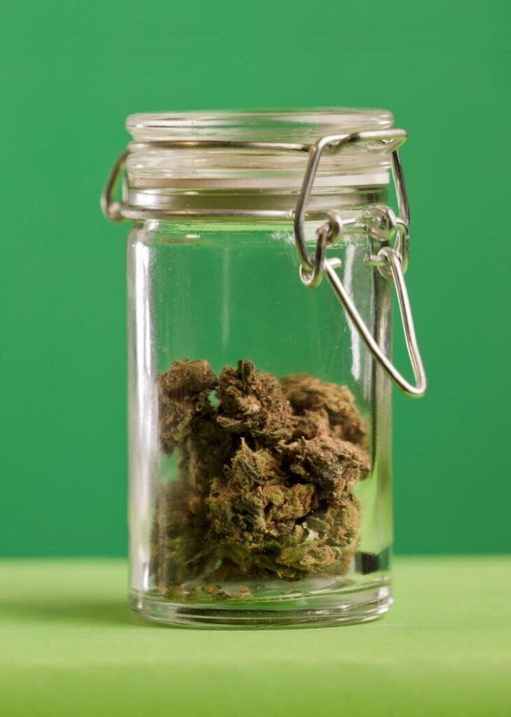 A glass jar filled with dried cannabis buds against a green background.